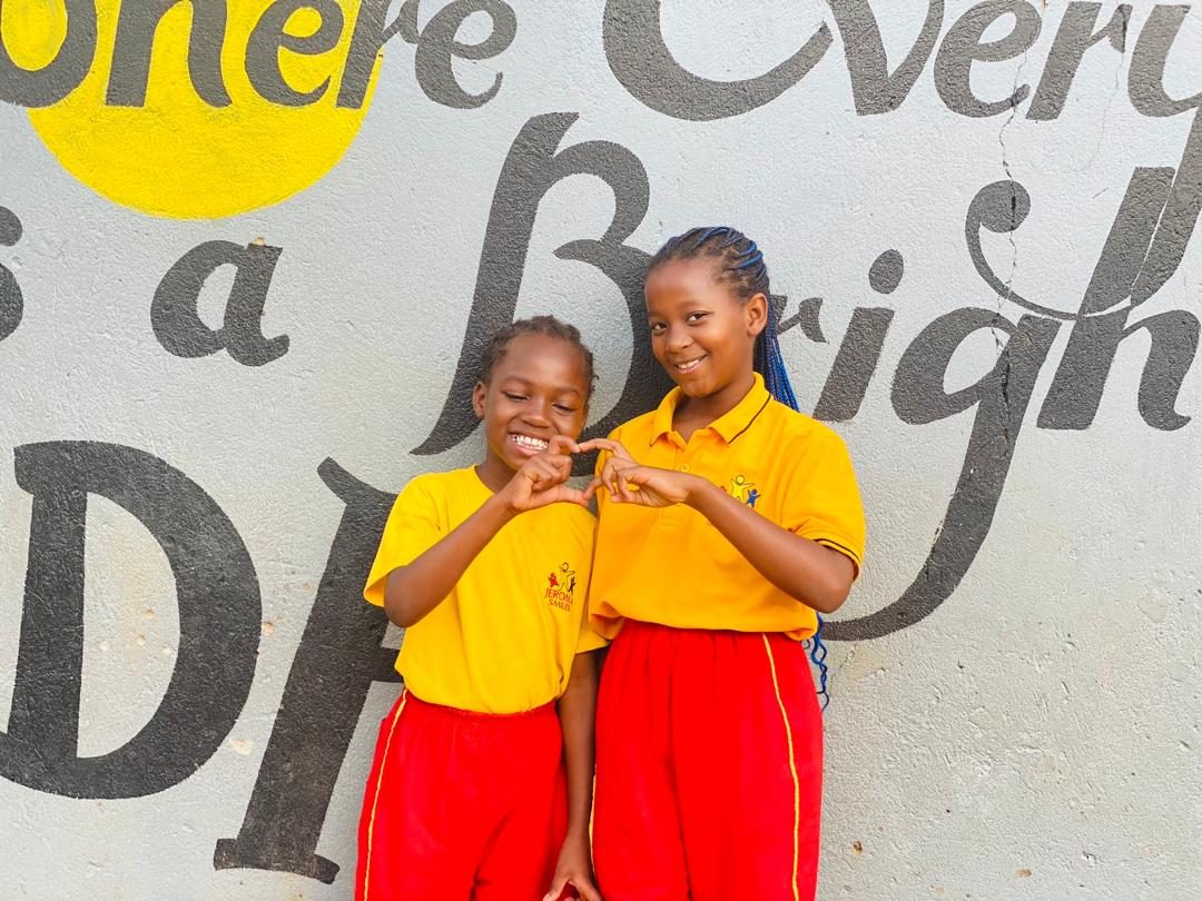 Pupils of Jeroma Smiles standing in front of the school motto wall